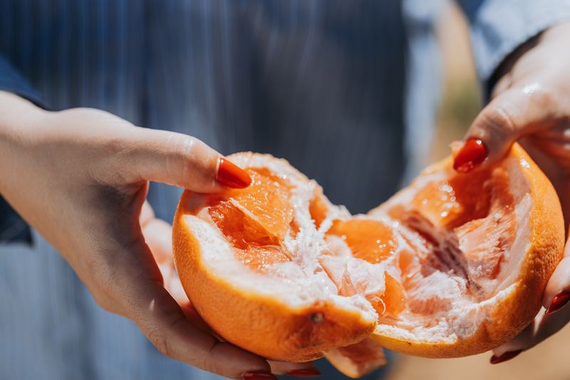 Two hands breaking a citrus fruit open, the pith and segments close up.
