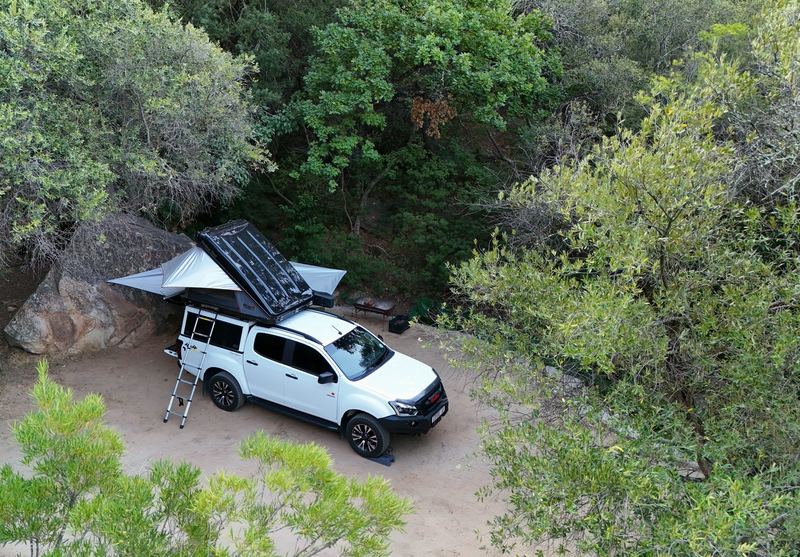 A camping site at The Baths seen from above, a vehicle with a rooftop tent under the trees beside a large boulder.