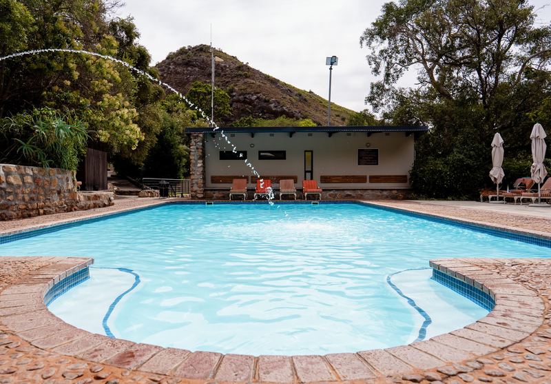The main swimming pool at The Baths, fed by a fountain, with the changing building and a rocky hill behind.