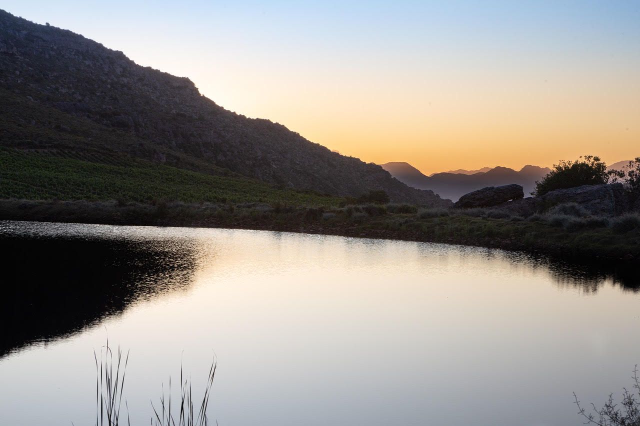 The dam at Tierhoek at dusk, the mountains in silhouette and an orange sky mirrored in the water
