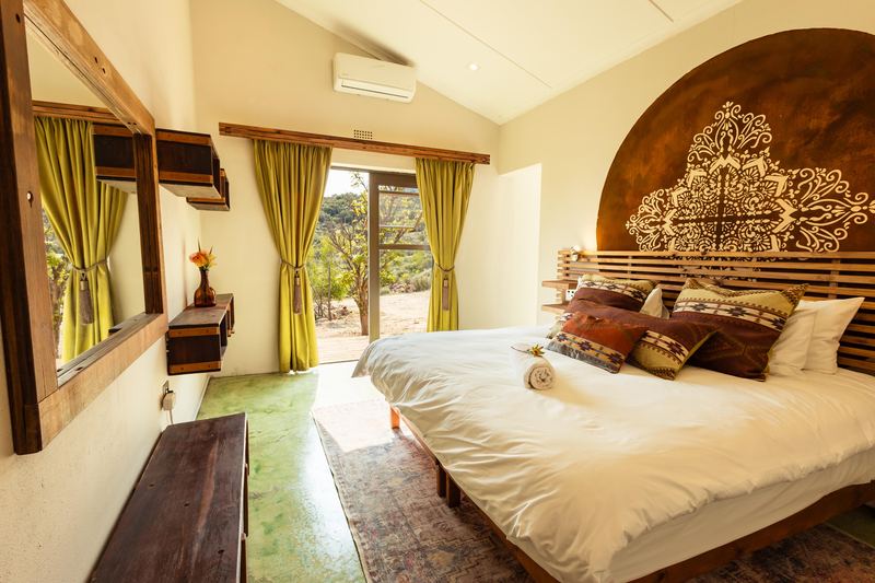The main bedroom at Boegoe, with a carved headboard and windows onto the bush.