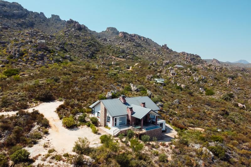 Aerial view across Wolfkop Nature Reserve: fynbos slopes rising to rocky Cederberg ridges, one house below.