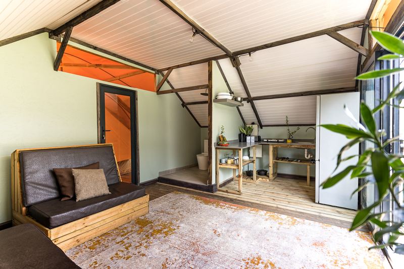 The open-plan living area of a villa, with a couch, a kitchen corner and the canvas roof overhead.